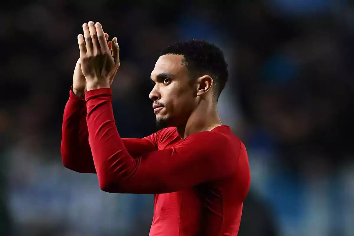 A soccer player in a red jersey applauds in a stadium. A soccer player in a red jersey applauds in a stadium.