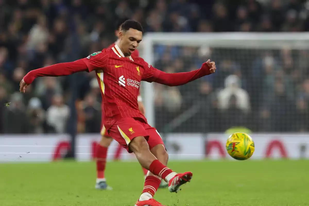 Un jugador de fútbol con uniforme rojo patea un balón en un estadio durante un partido. Un jugador de fútbol con uniforme rojo patea un balón en un estadio durante un partido.