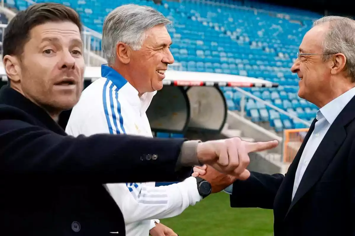 Tres hombres conversan y se saludan en un estadio de fútbol.