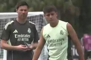 Two people wearing Real Madrid training gear are on a soccer field; one of them appears to be a coach and the other a player.