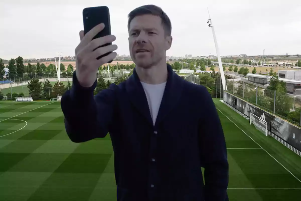 A man holding a mobile phone in front of a soccer field.