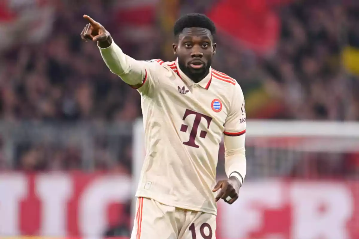 Jugador de fútbol con uniforme claro del Bayern Múnich señalando hacia adelante en un estadio.