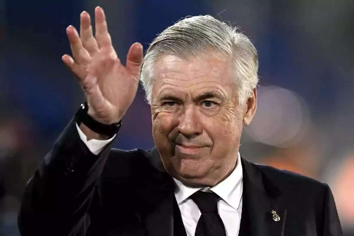 A gray-haired man in a dark suit waves. A gray-haired man in a dark suit waves.
