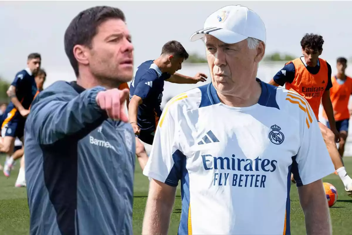 Two soccer coaches on a training field with players practicing in the background.