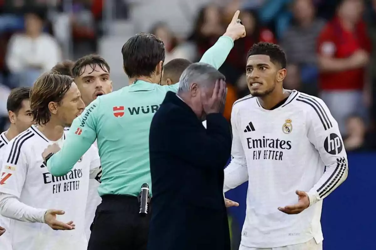 Un árbitro discute con jugadores de fútbol mientras un hombre en el frente se cubre la cara con la mano en un gesto de frustración.