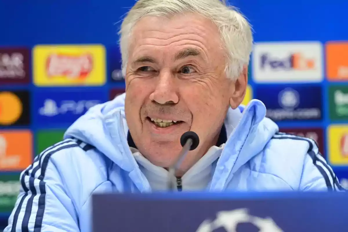 A smiling man at a press conference against a background of sports sponsor logos.