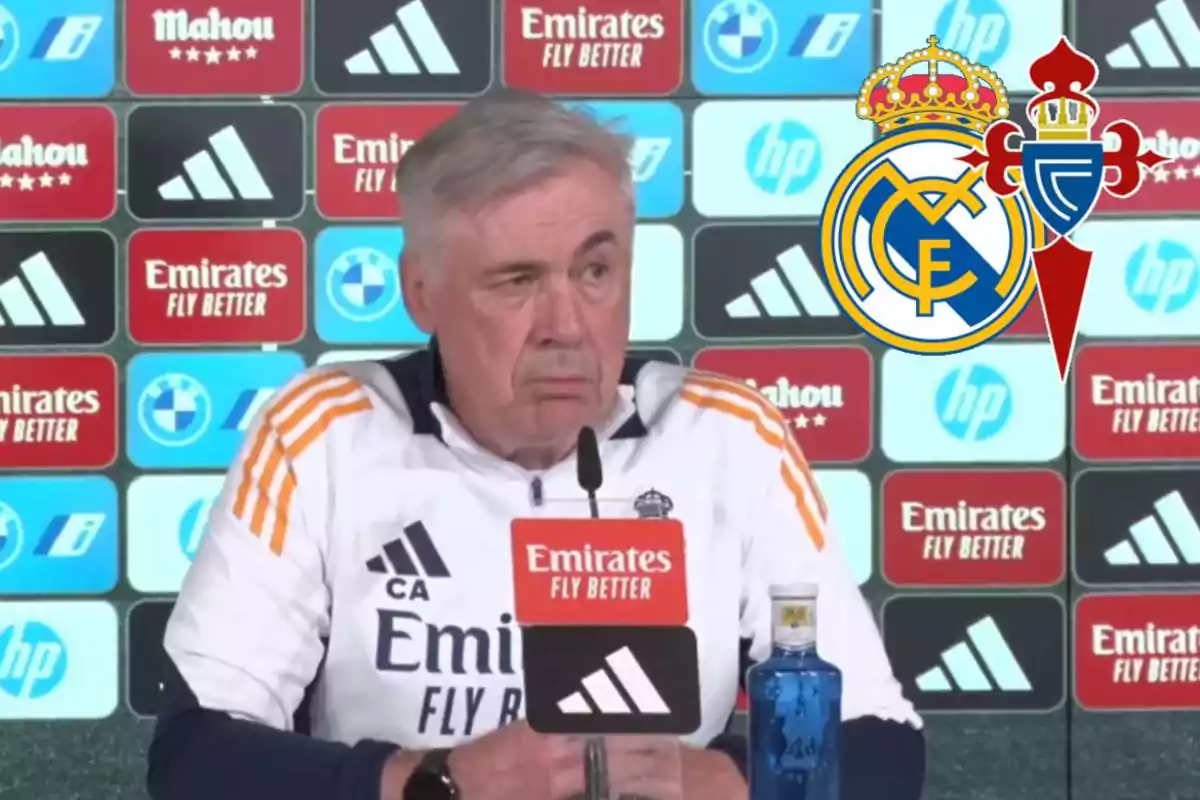 A soccer coach at a press conference with sponsor logos and team crests in the background.