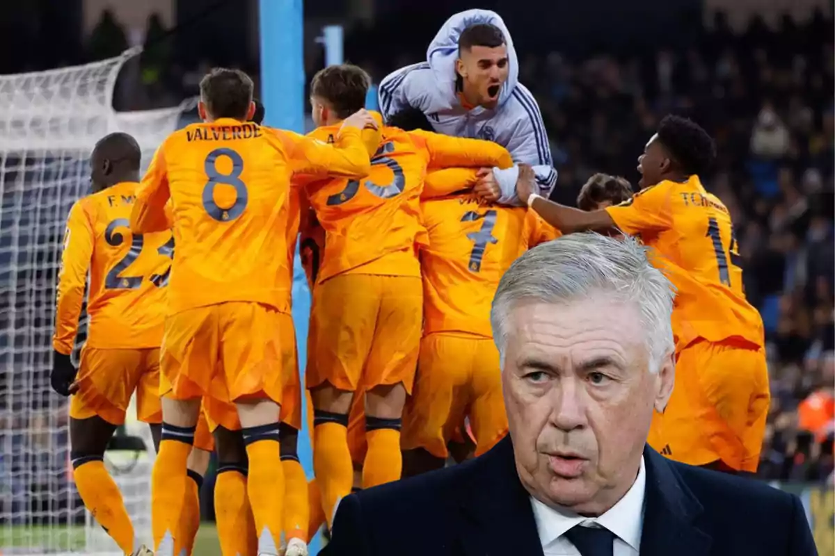 A group of players in orange uniforms celebrates a goal while a gray-haired man appears in the foreground.