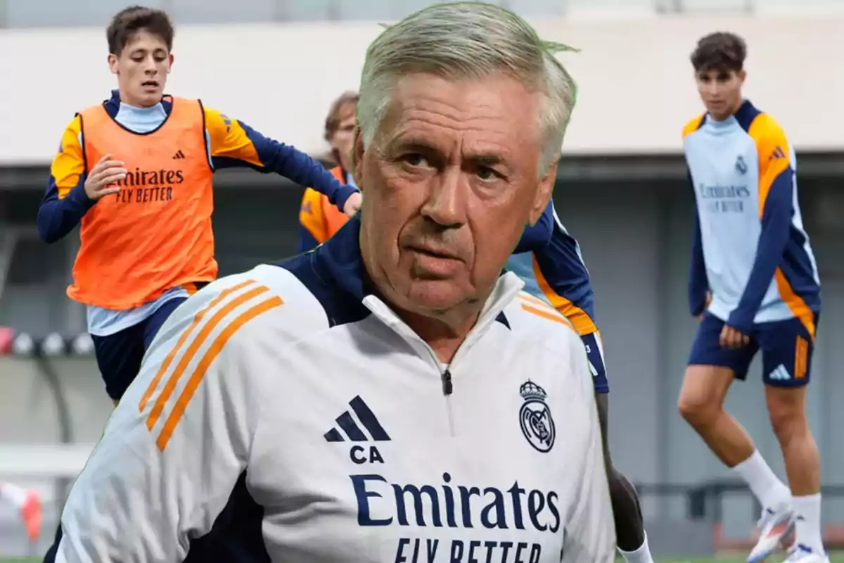 A soccer coach in Real Madrid training gear looks on as several players practice on the field.