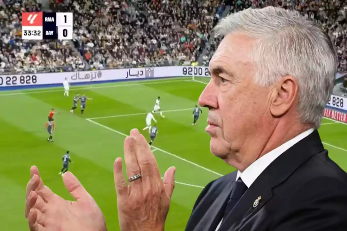 A coach claps while watching a soccer game in a stadium full of spectators.