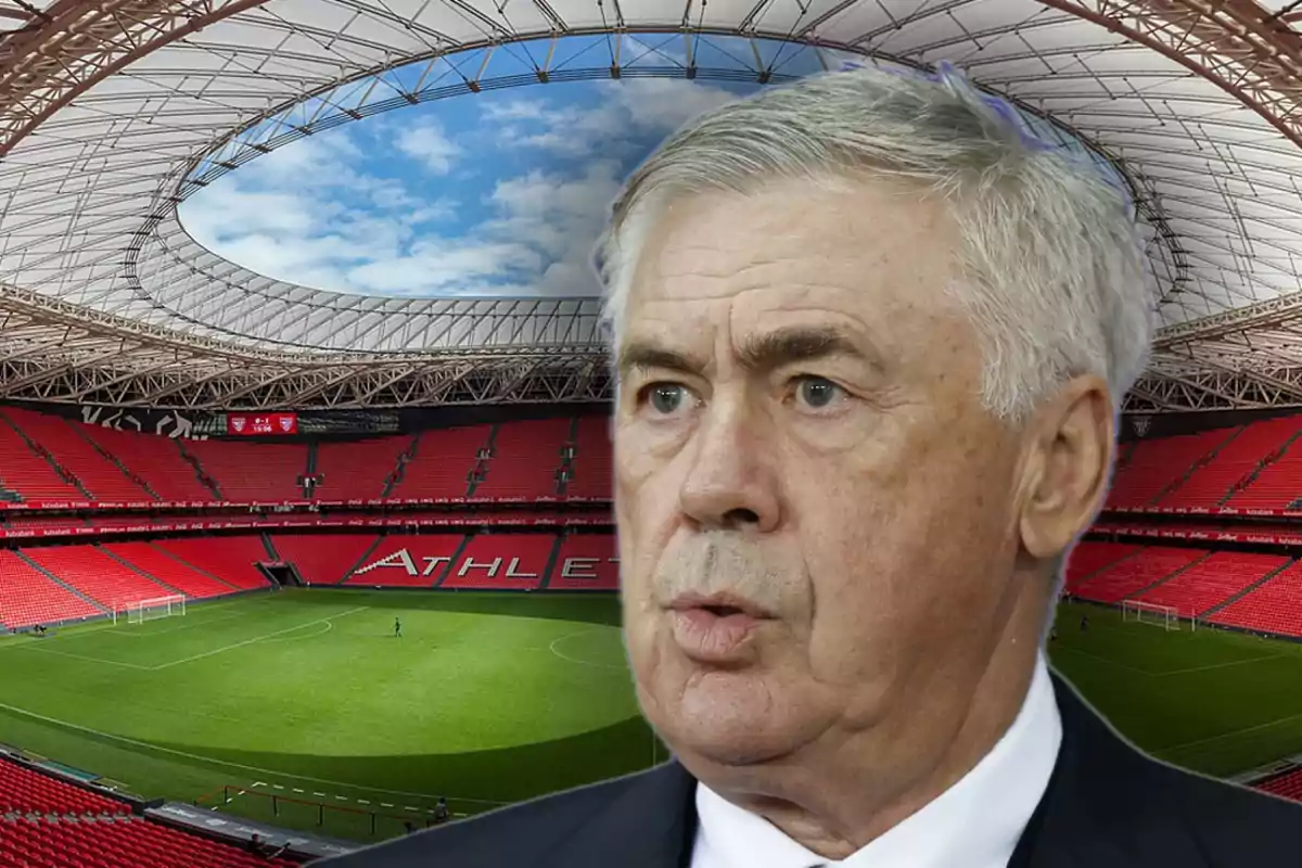 Un hombre de cabello canoso en primer plano con un estadio de fútbol vacío de fondo.