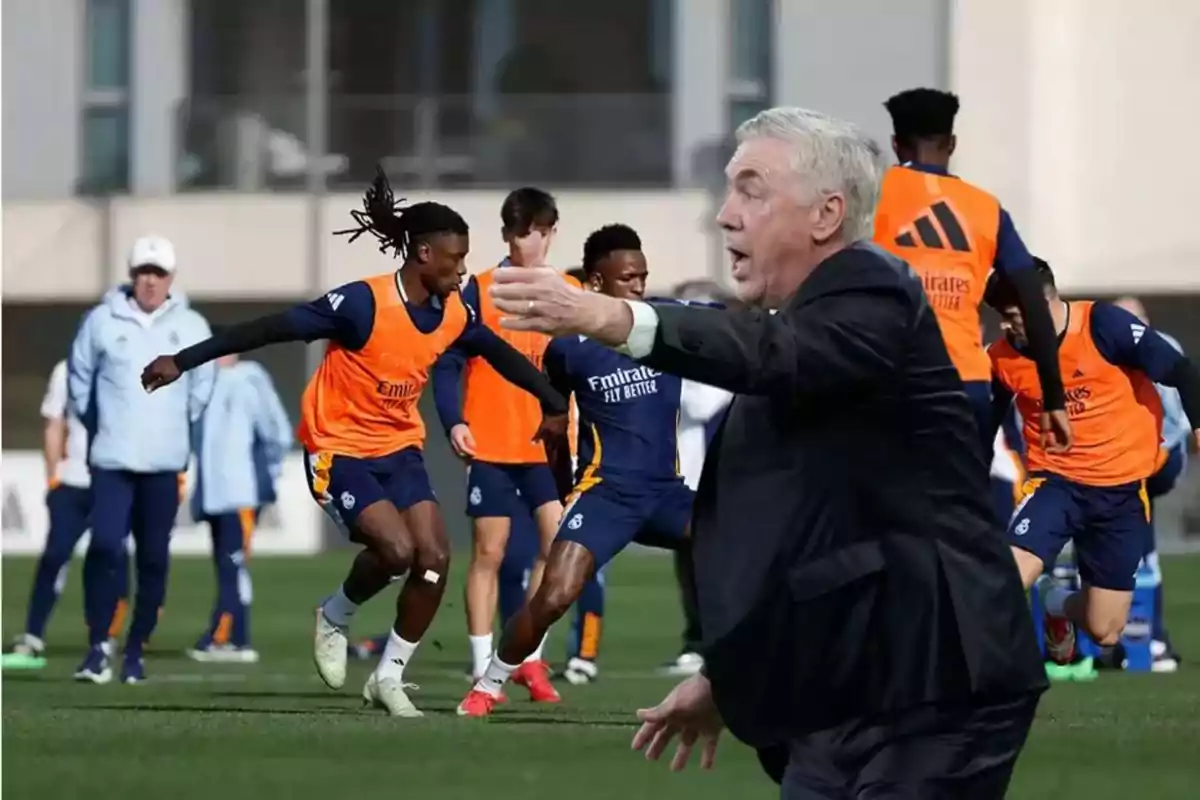 A soccer coach gestures while the players train on the field.