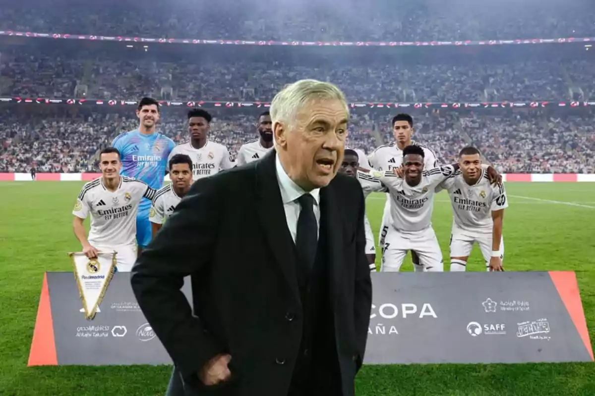 Un entrenador de fútbol en traje oscuro está frente a un grupo de jugadores uniformados en un estadio lleno de espectadores.