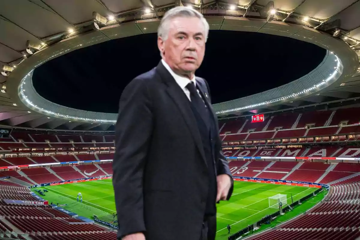 A man in a dark suit is standing in an empty football stadium lit up at night.