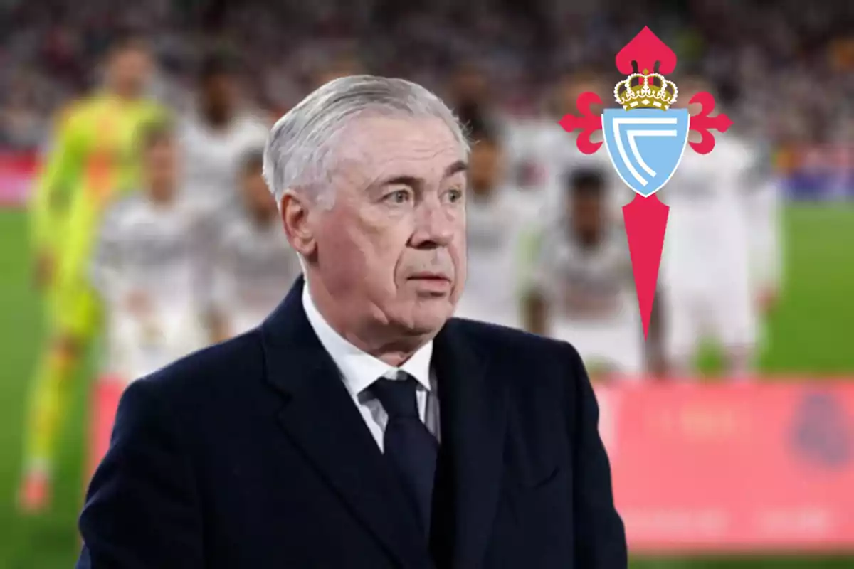A gray-haired man in a dark suit is on a soccer field with a team logo in the background.