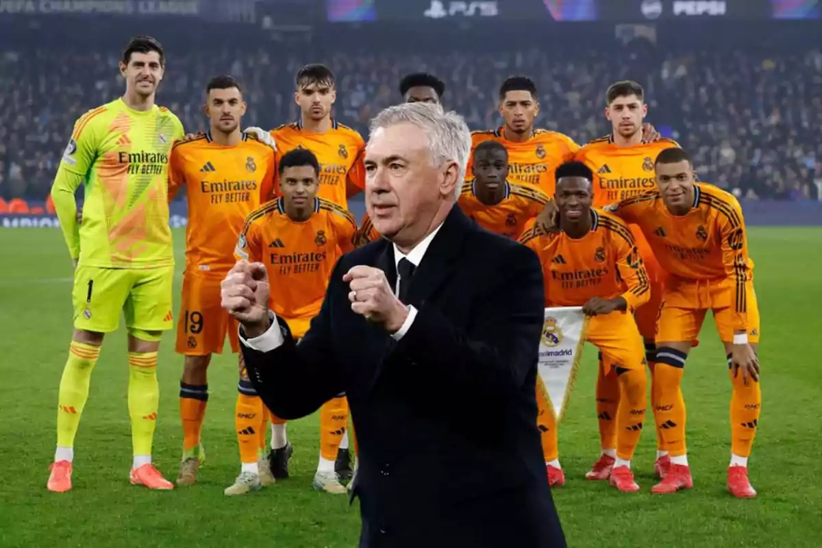 A soccer coach is standing in front of a group of players on the field, all wearing orange uniforms.