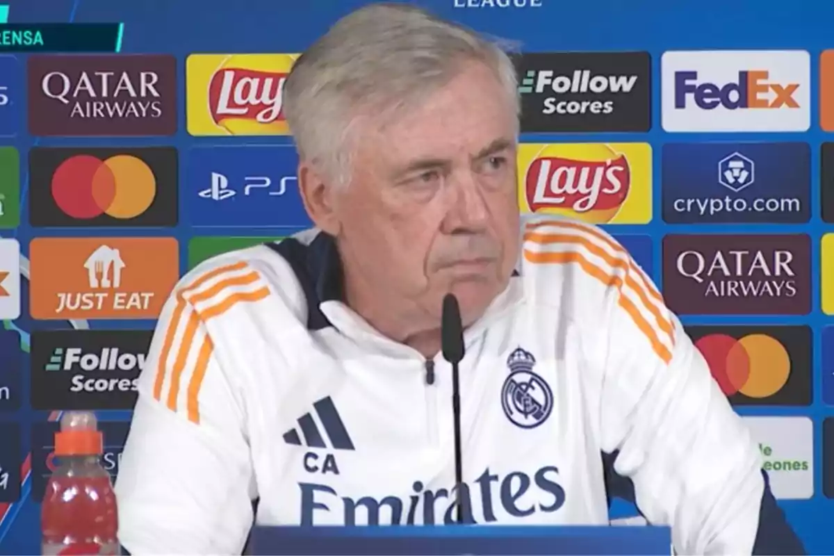 A man at a press conference against a backdrop of sports sponsor logos.