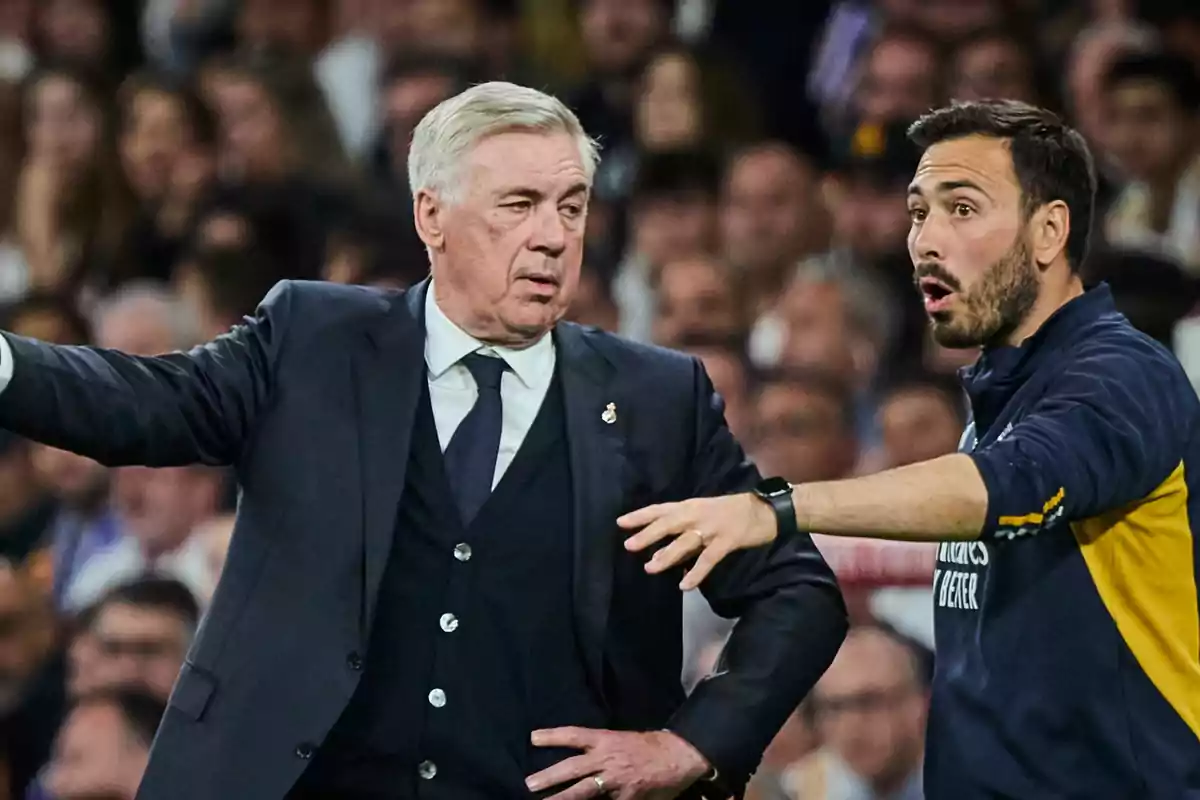 Dos hombres en un campo de fútbol discutiendo estrategias durante un partido.