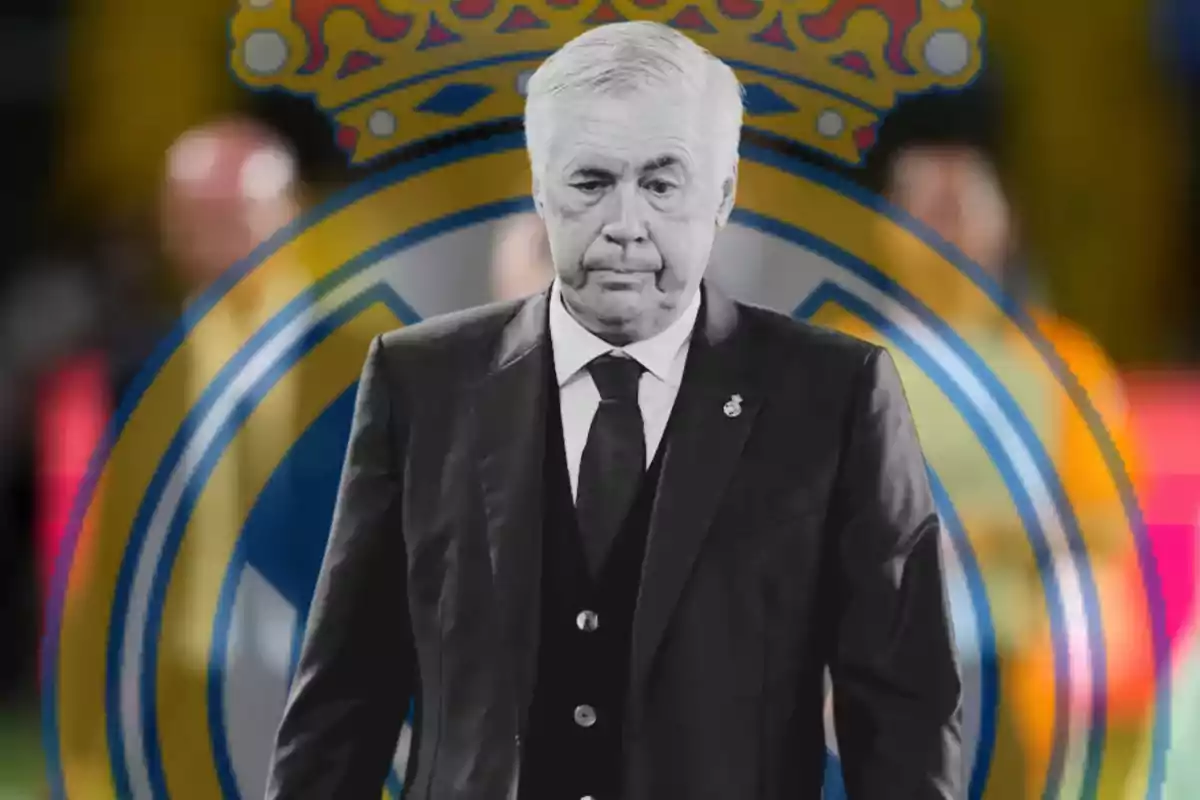 Un hombre de cabello canoso y traje oscuro está frente a un escudo de un equipo de fútbol.
