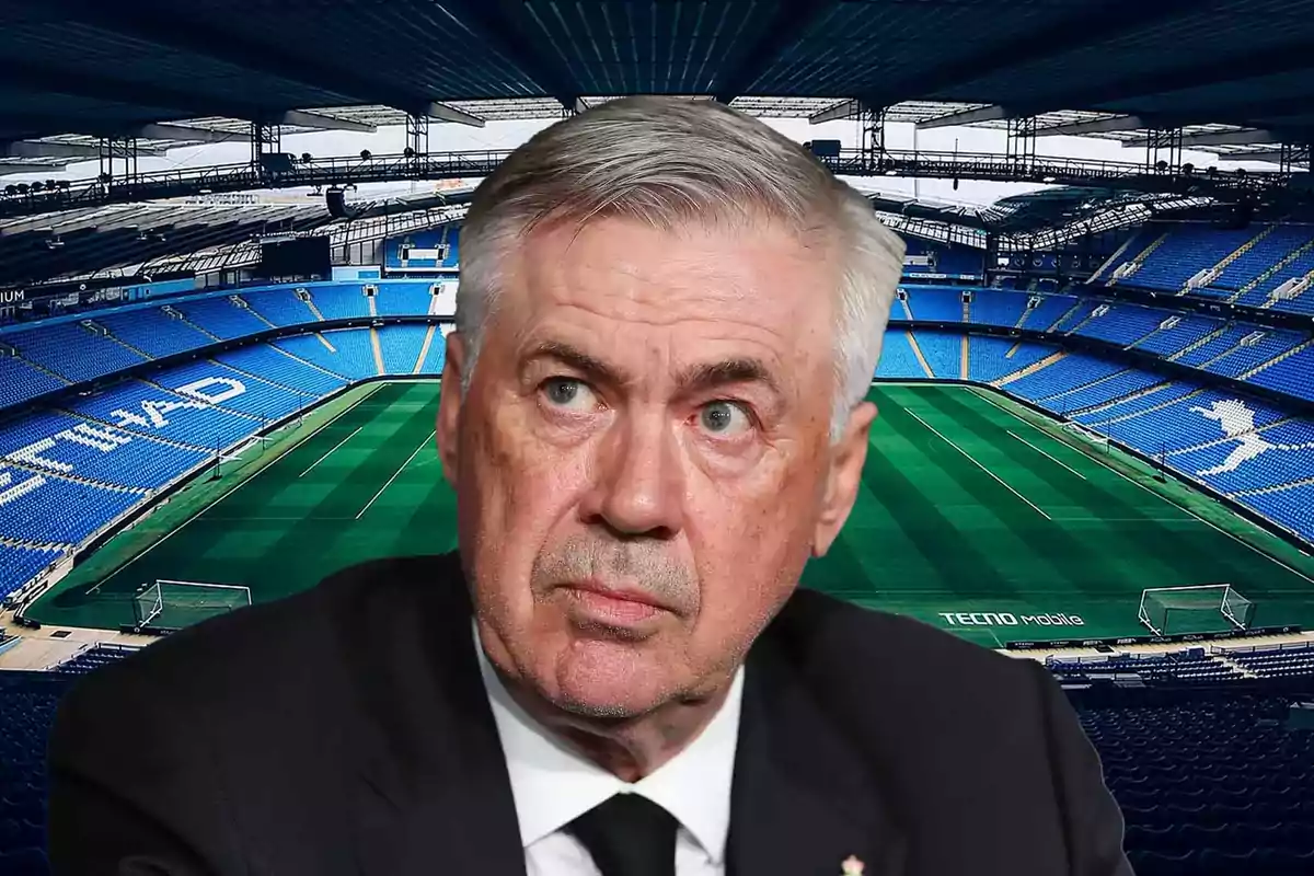 A gray-haired man with a serious expression in front of an empty football stadium.