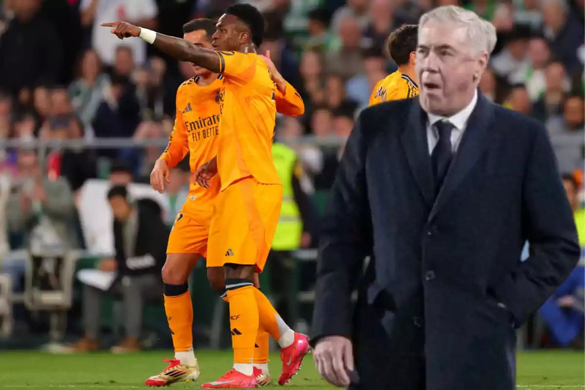 A group of players in orange uniforms celebrating on the field while a man in a dark coat watches from the front.