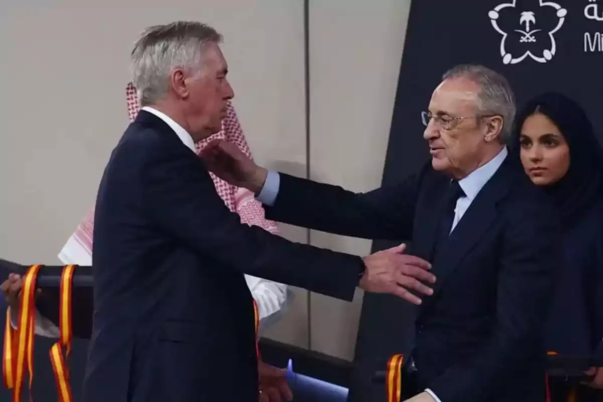Two men in suits greet each other cordially while a woman in a hijab watches in the background. Two men in suits greet each other cordially while a woman in a hijab watches in the background.