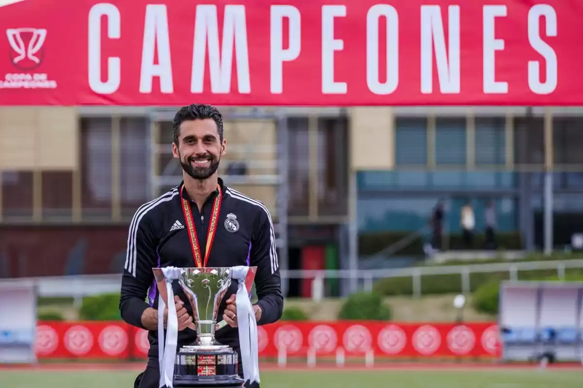 Un hombre sonriente sostiene un trofeo frente a un cartel rojo que dice Un hombre sonriente sostiene un trofeo frente a un cartel rojo que dice