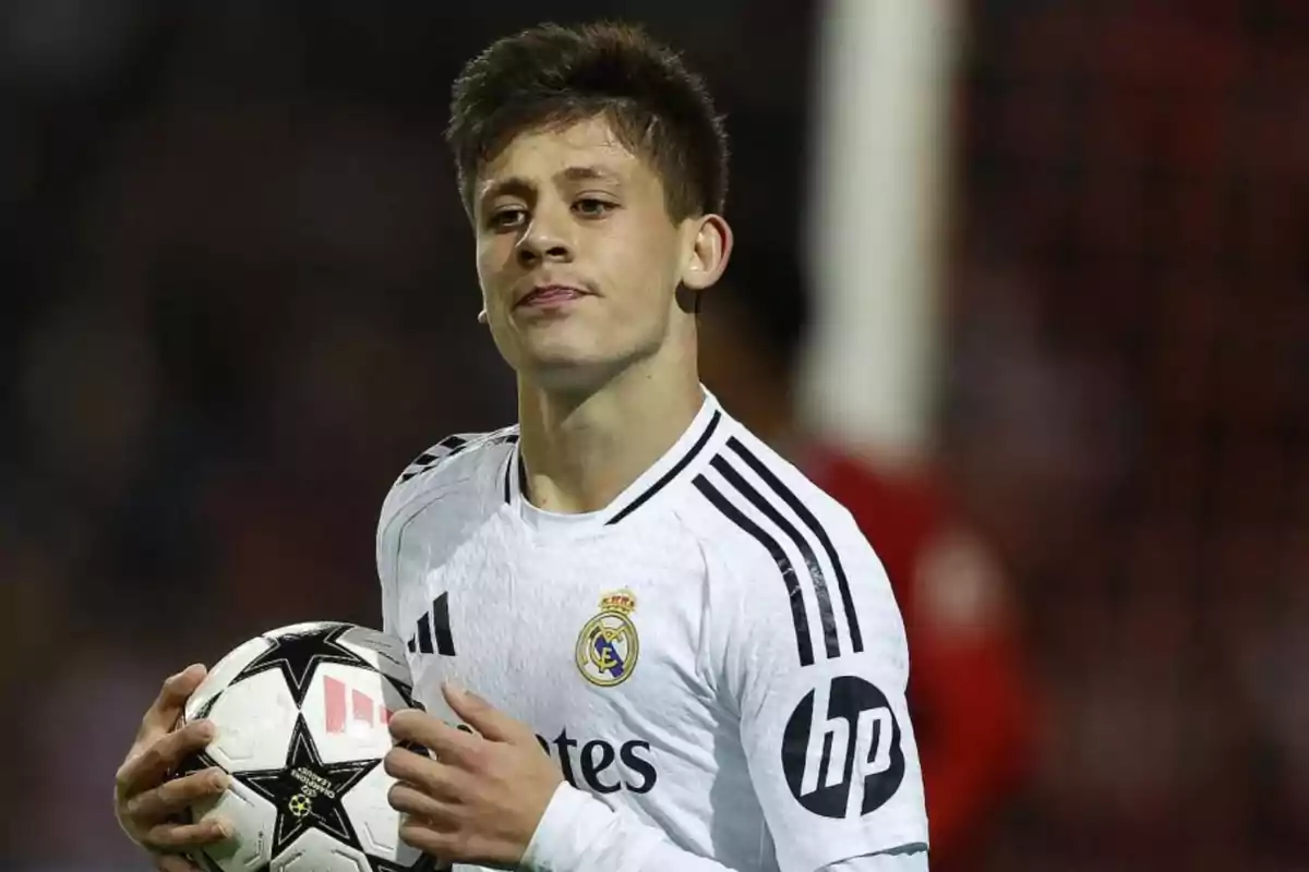 Jugador de fútbol con uniforme blanco sosteniendo un balón en el campo.