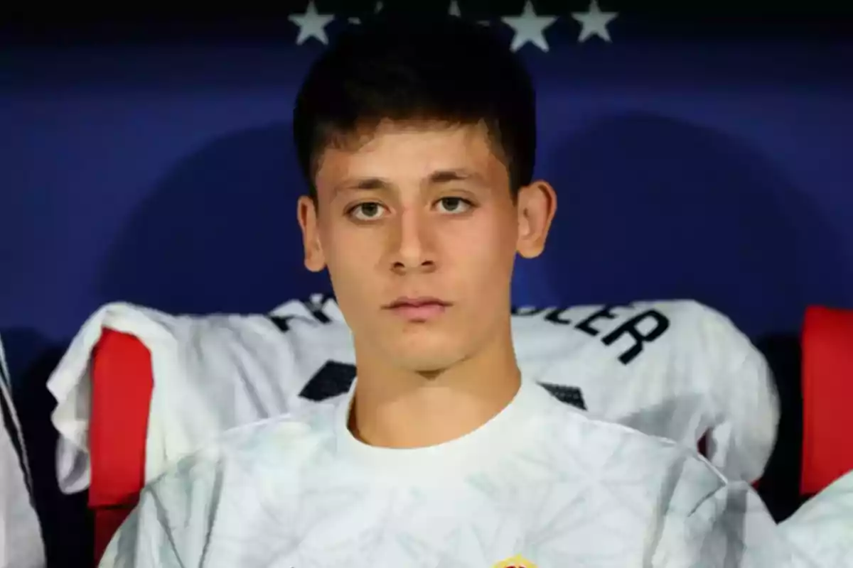 Un joven con camiseta blanca sentado frente a un fondo azul con estrellas.