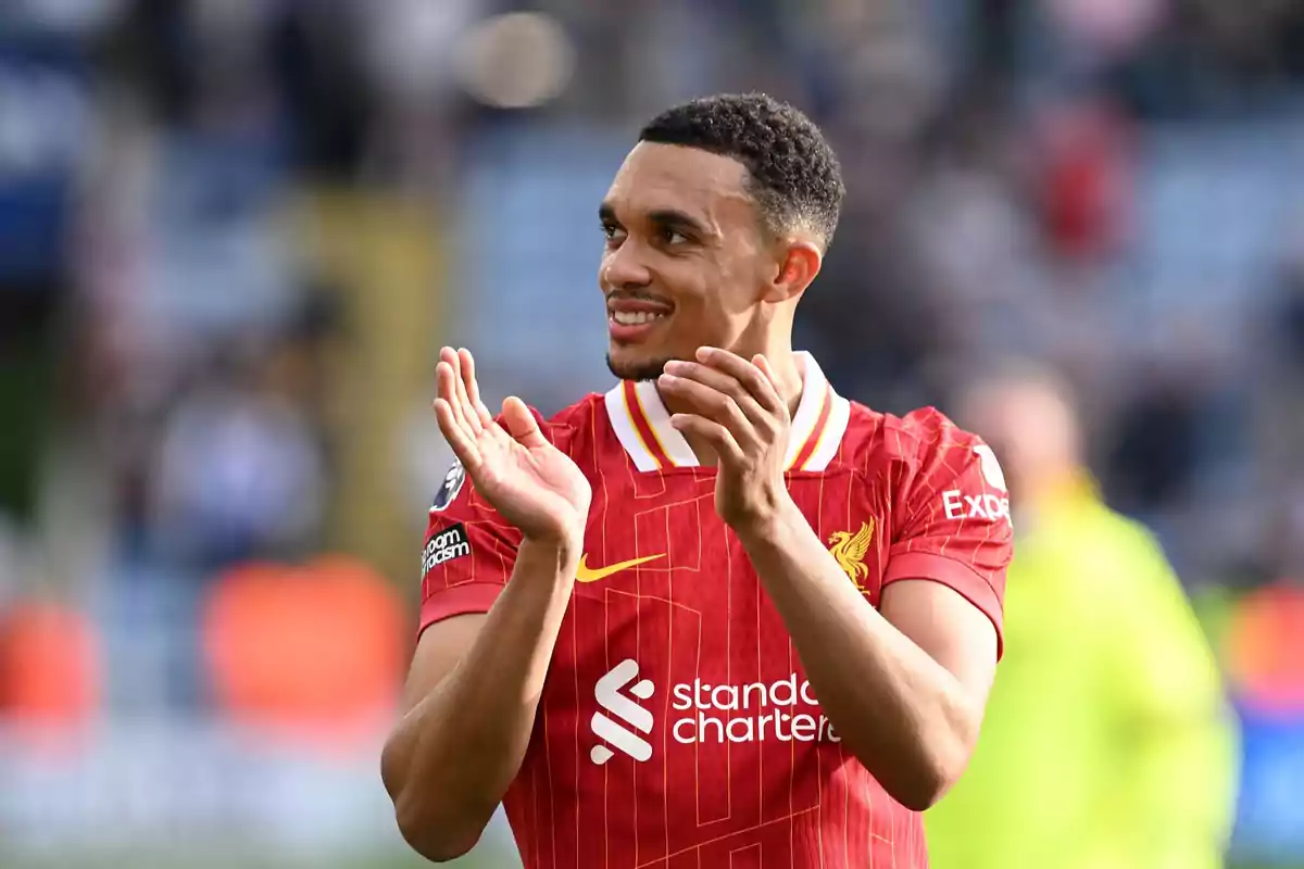 Un jugador de fútbol aplaudiendo mientras viste un uniforme rojo con detalles amarillos y un logotipo de patrocinador visible. Un jugador de fútbol aplaudiendo mientras viste un uniforme rojo con detalles amarillos y un logotipo de patrocinador visible.