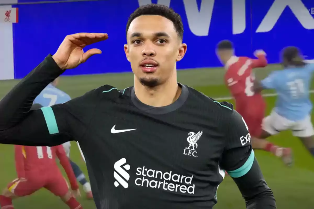 A player in a black Liverpool FC uniform gestures with his hand on his forehead, while a game is in progress in the background.