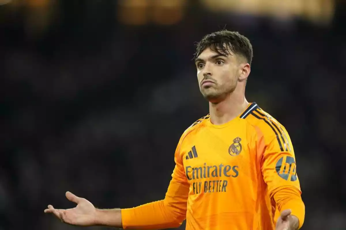 Un jugador de fútbol con uniforme naranja del Real Madrid con los brazos extendidos en un gesto de confusión o pregunta durante un partido. Un jugador de fútbol con uniforme naranja del Real Madrid con los brazos extendidos en un gesto de confusión o pregunta durante un partido.