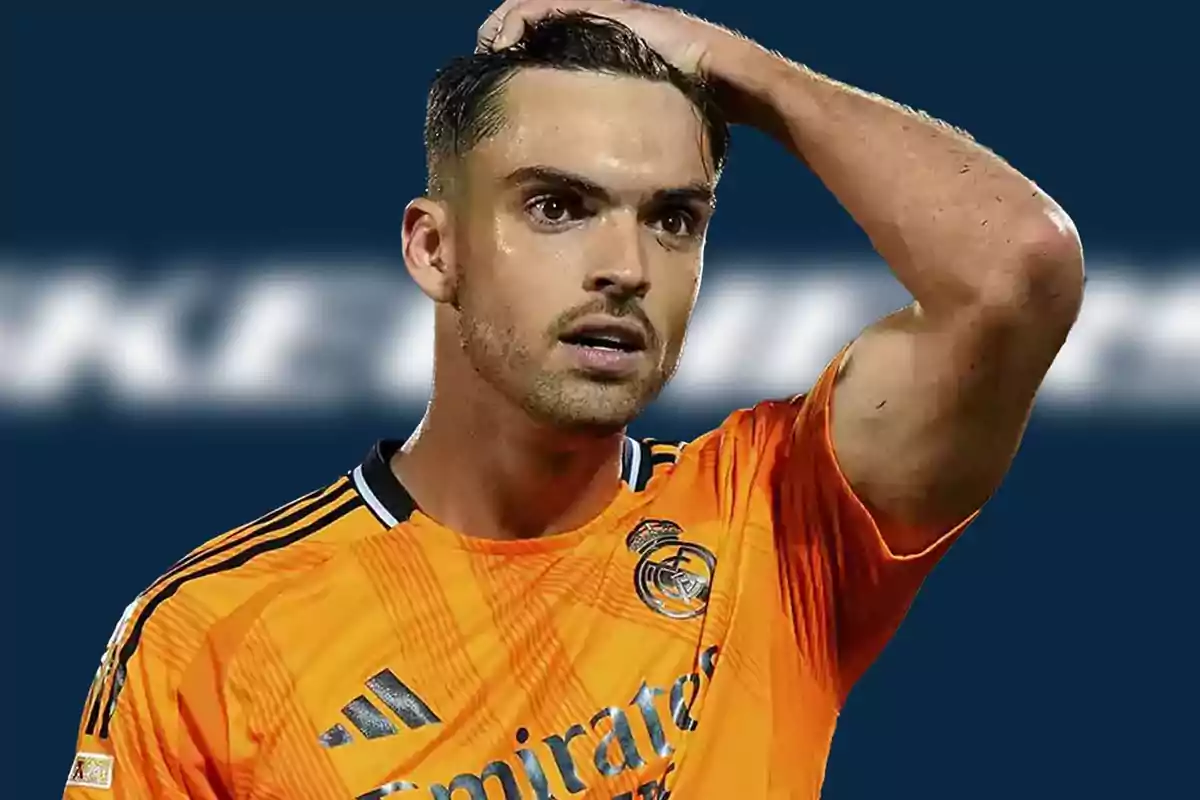 A soccer player in an orange Real Madrid uniform touches his head with a thoughtful expression.