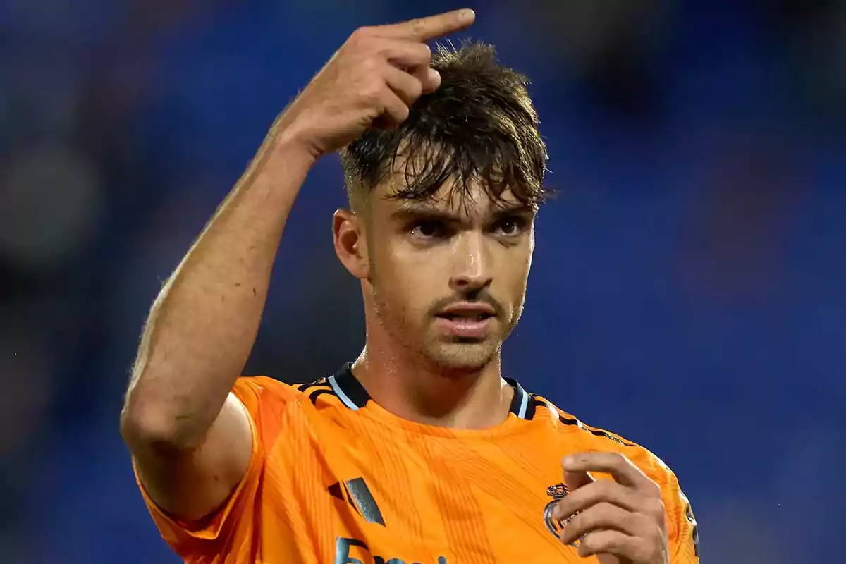 A soccer player in an orange jersey points upward during a game. A soccer player in an orange jersey points upward during a game.
