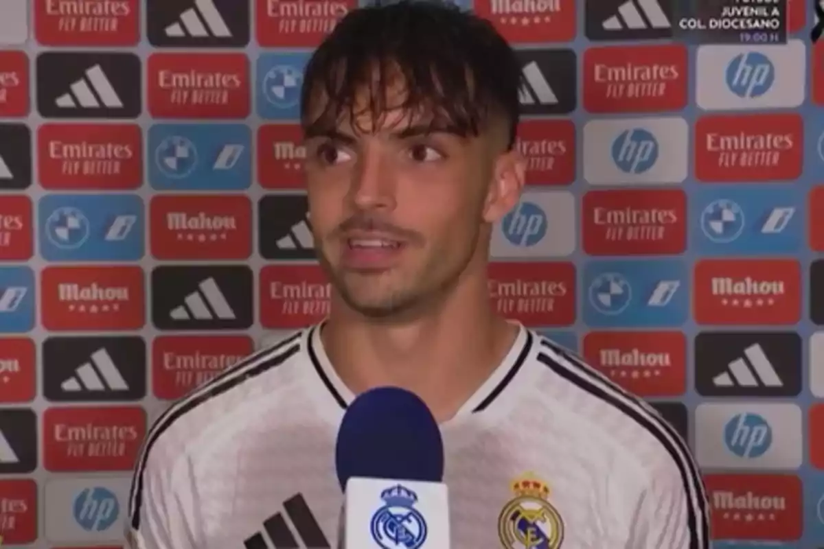 A Real Madrid soccer player gives an interview in front of a background with sponsor logos.