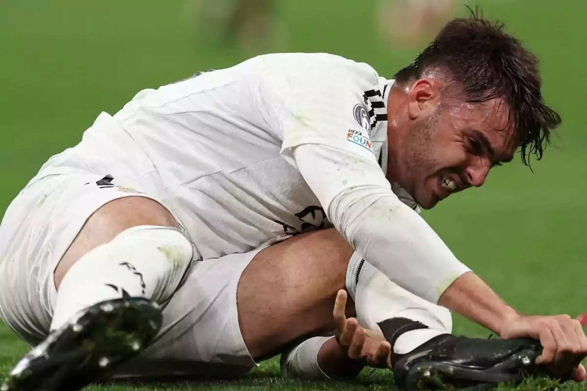 Un jugador de fútbol en el suelo con expresión de dolor mientras sostiene su pierna.