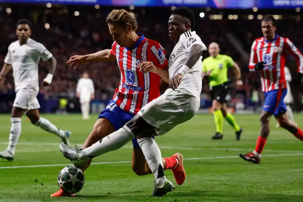 Dos jugadores de fútbol compiten por el balón en un partido, uno con uniforme a rayas rojas y blancas y el otro de blanco, mientras un árbitro observa la jugada.