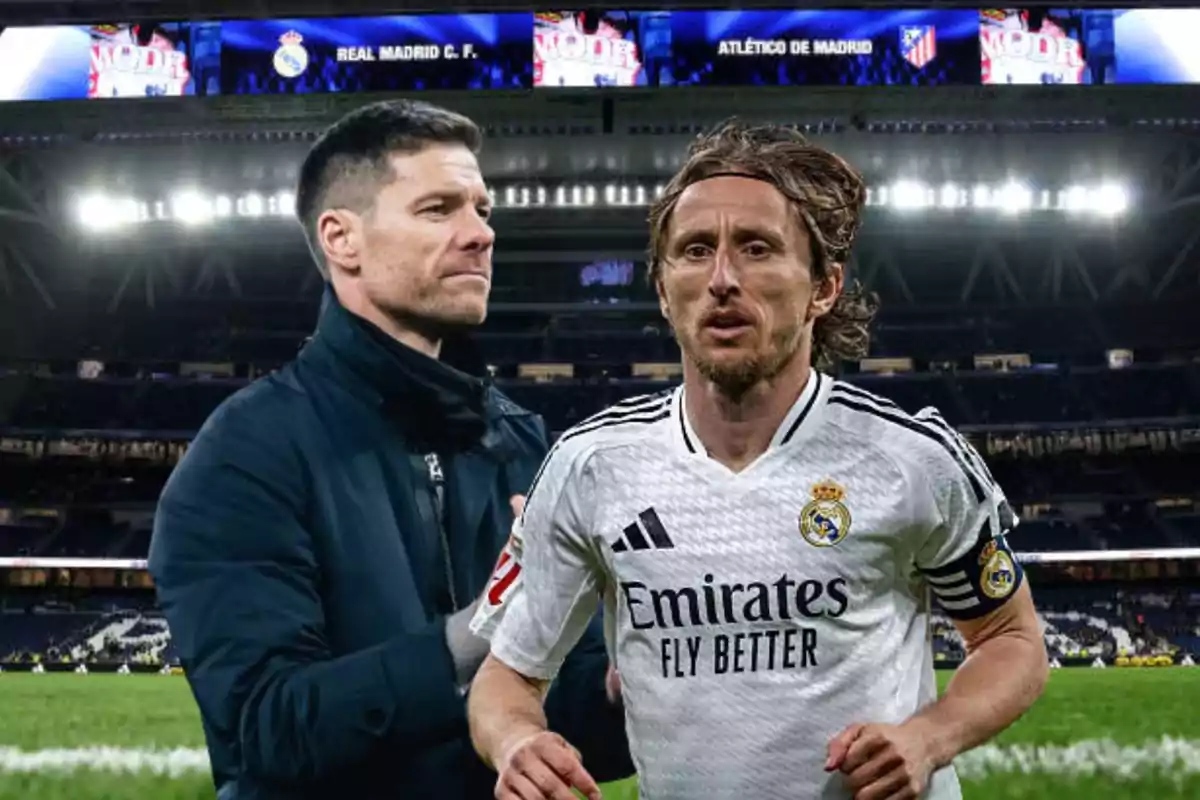 Un jugador de fútbol del Real Madrid en el campo con un entrenador al fondo en un estadio iluminado.