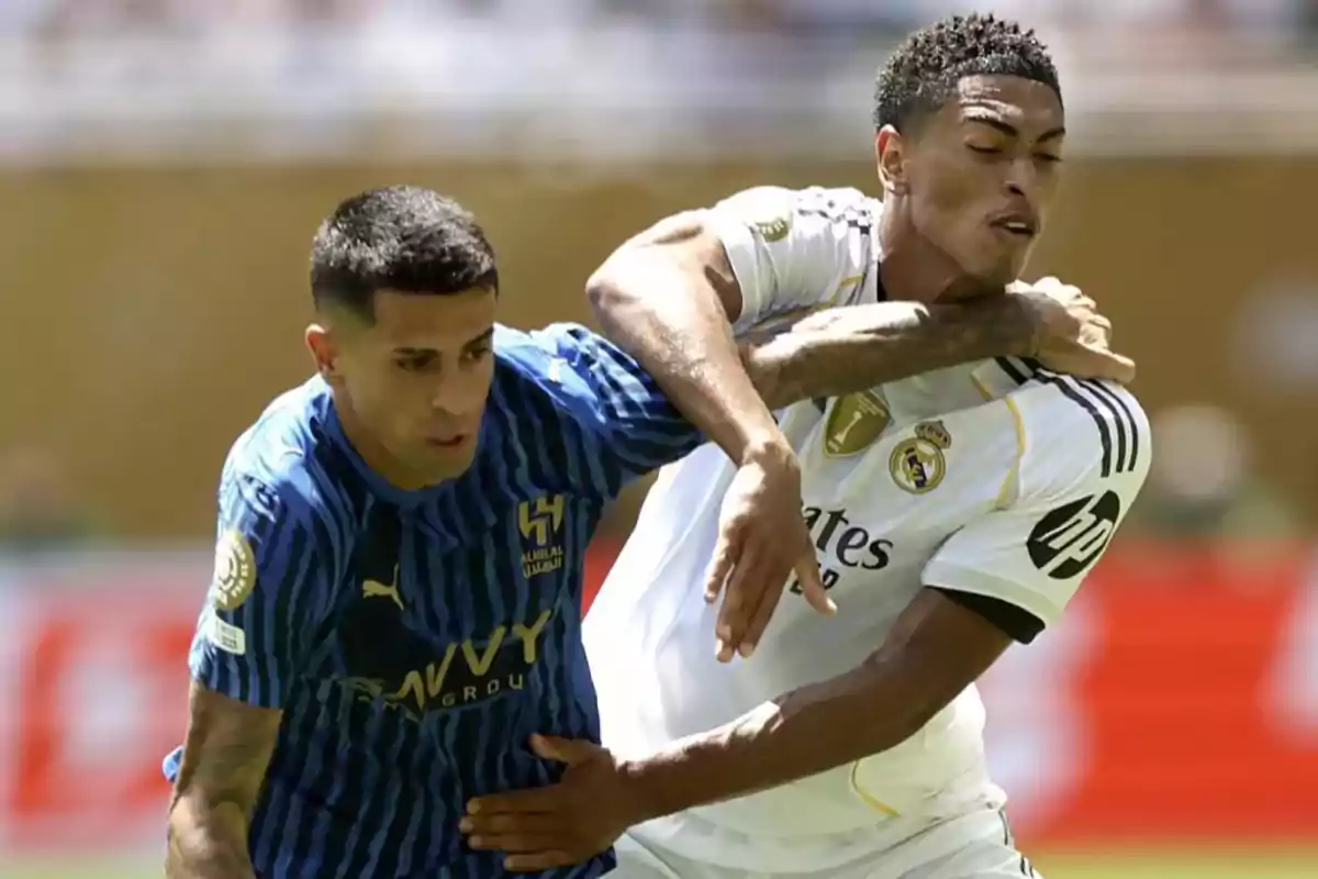 Dos futbolistas disputan el balón durante un partido uno con uniforme azul y el otro con uniforme blanco