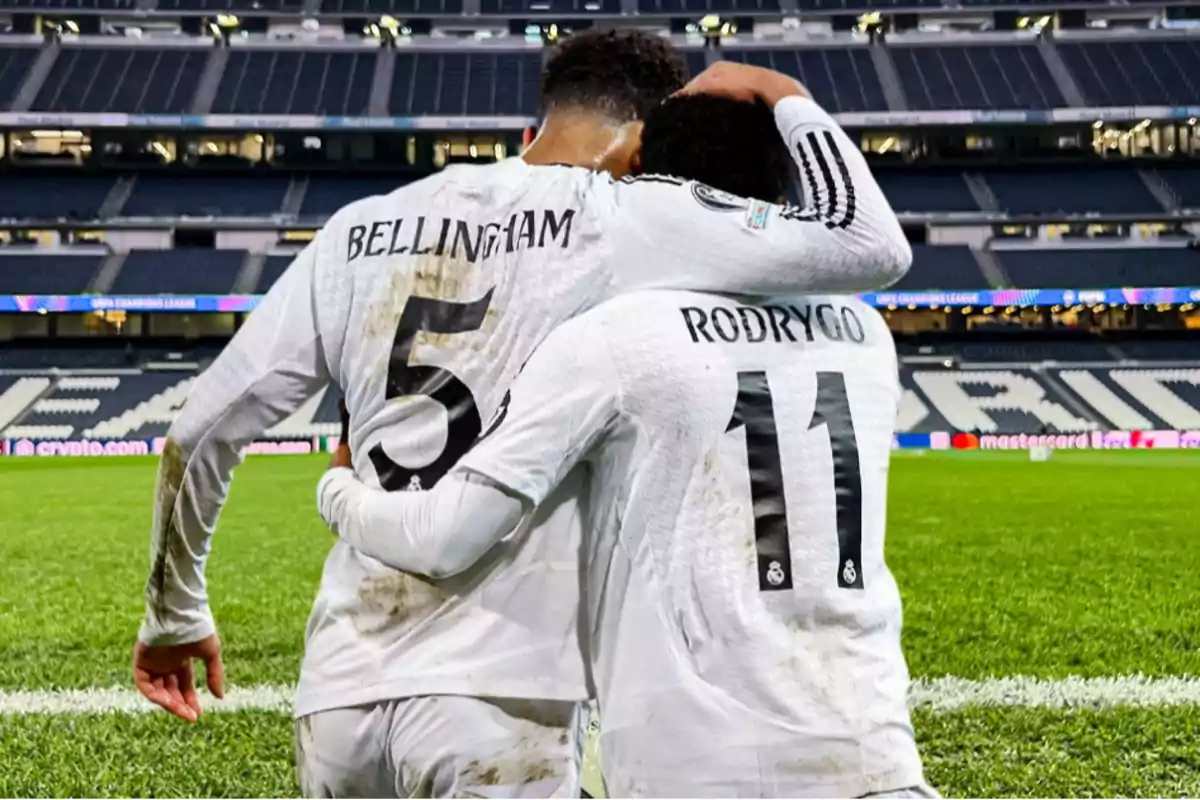 Dos jugadores de fútbol con uniformes blancos se abrazan en el campo de juego, mostrando los números 5 y 11 en sus camisetas.