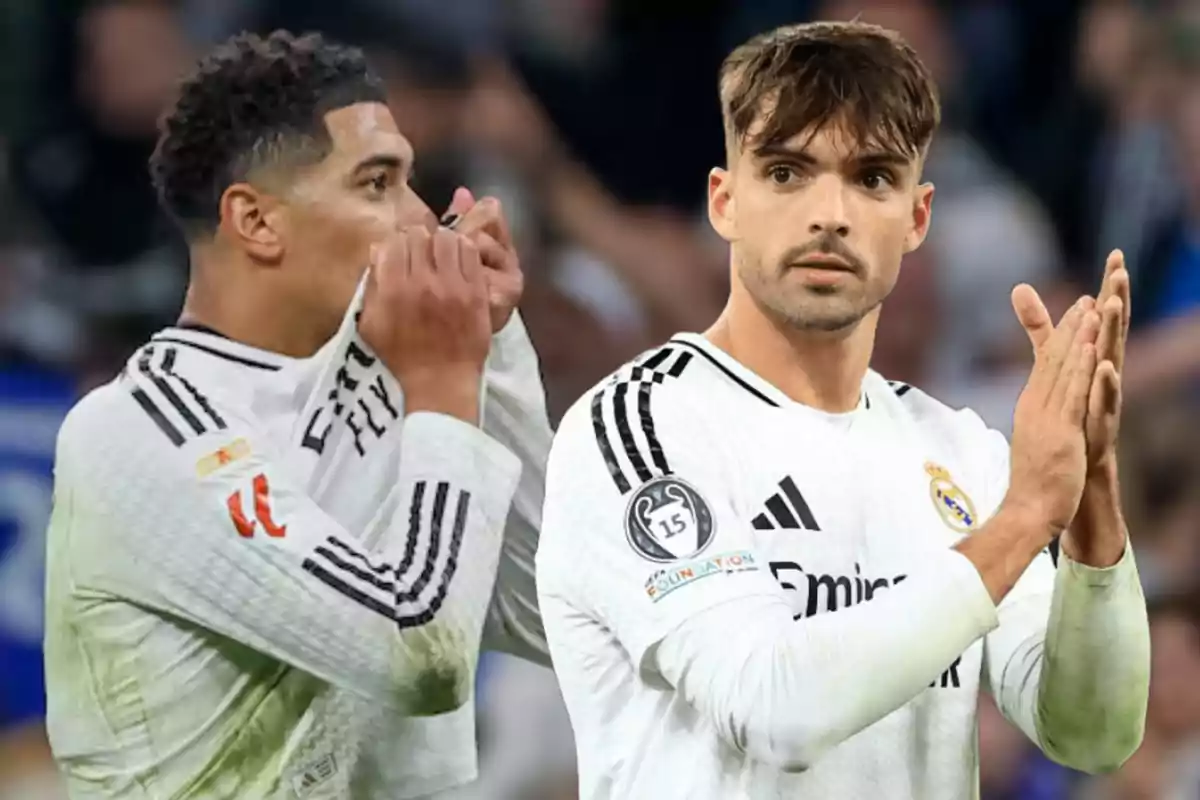 Dos jugadores de fútbol con uniformes blancos en el campo, uno besa el escudo de su camiseta y el otro aplaude.