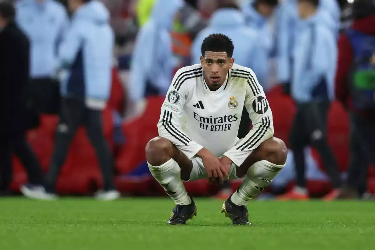 A Real Madrid soccer player crouching on the field with people out of focus in the background.