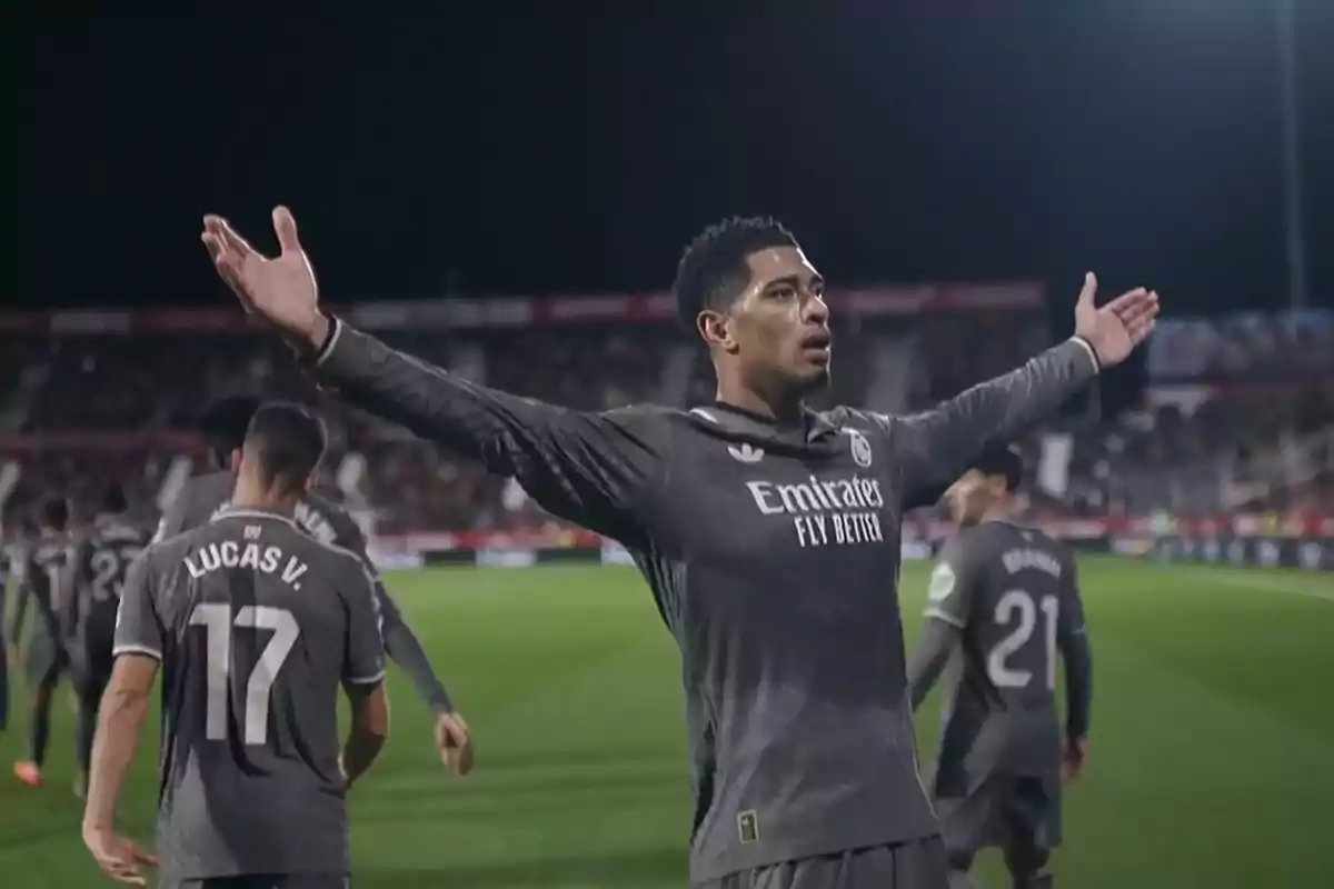 A soccer player with his arms outstretched celebrates on the field as other players walk behind him.