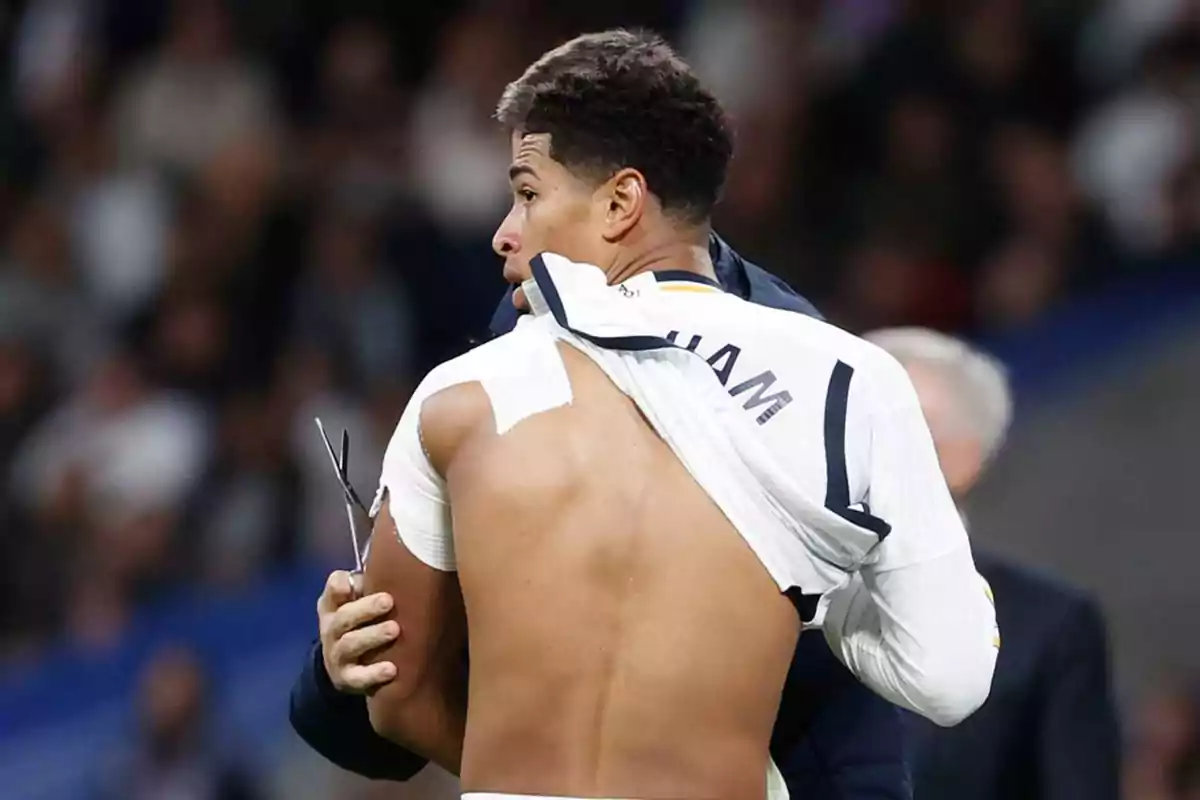 A player with his jersey lifted showing his back while being attended to by a person with scissors.