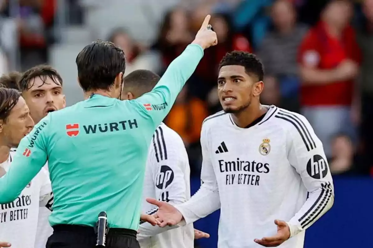 A referee points with his finger while a Real Madrid player gestures with his hands in a soccer match.