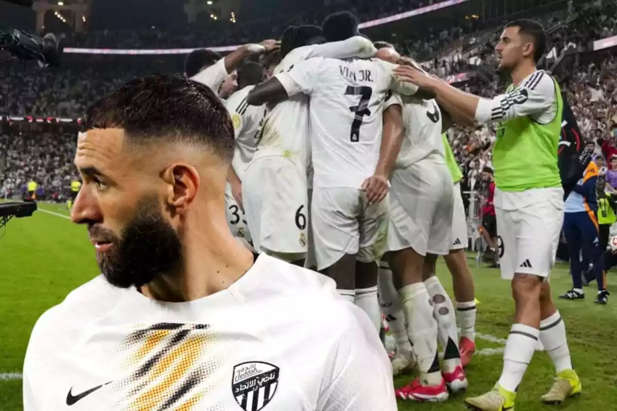 Un jugador de fútbol con barba y cabello corto está en primer plano mientras un grupo de jugadores celebra en el campo de juego al fondo.