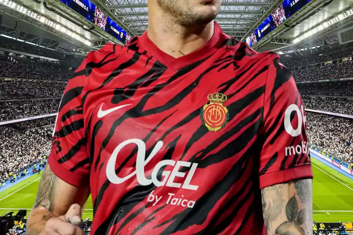 Un jugador de fútbol con un uniforme rojo y negro con diseño de rayas, en un estadio lleno de espectadores.