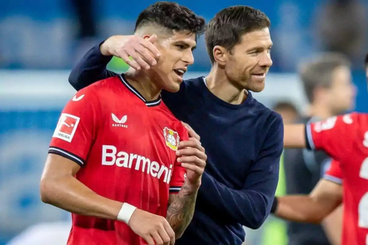 Two people wearing Bayer Leverkusen jerseys celebrate on a soccer field. Two people wearing Bayer Leverkusen jerseys celebrate on a soccer field.