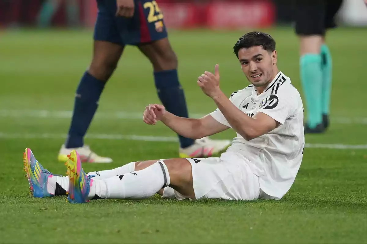 Soccer player in a white uniform sitting on the grass giving a thumbs-up during a match Soccer player in a white uniform sitting on the grass giving a thumbs-up during a match