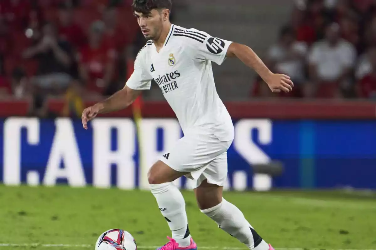 Jugador de fútbol con uniforme blanco controlando el balón en un campo de juego.